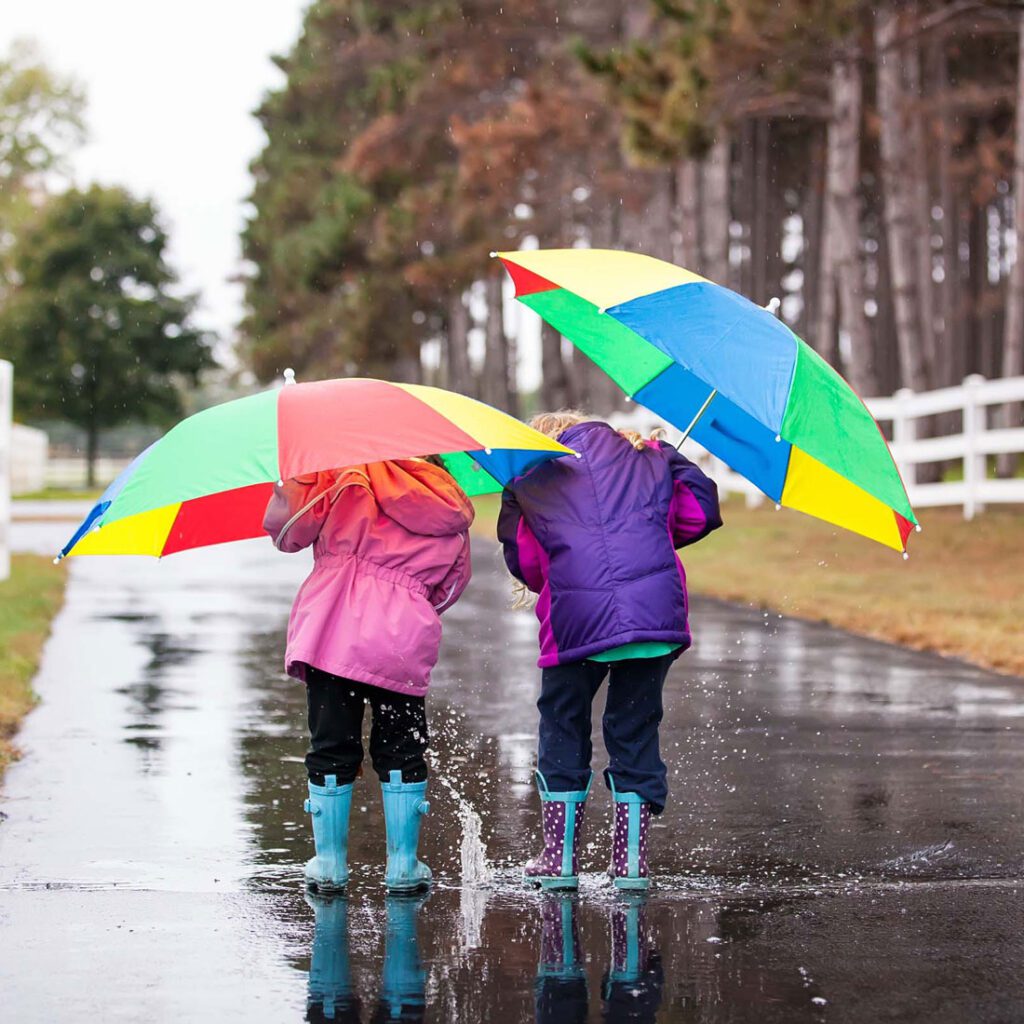 Two children in vibrant raincoats and wellies holding umbrellas, a snapshot of life when adopting siblings in the UK