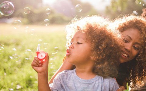 A child blowing bubbles with their guardian in a sunlit park, encapsulating the joyous moments in a UK adoptive family's day