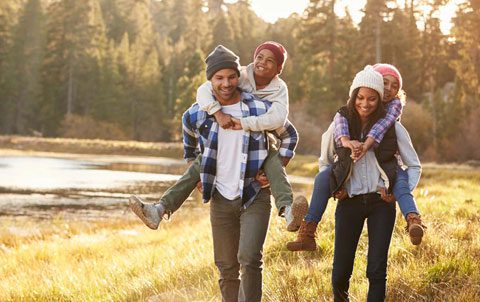 A family of adopted siblings enjoying a piggyback ride outdoors, laughter fills the air, highlighting the joy of family life after adoption in the UK