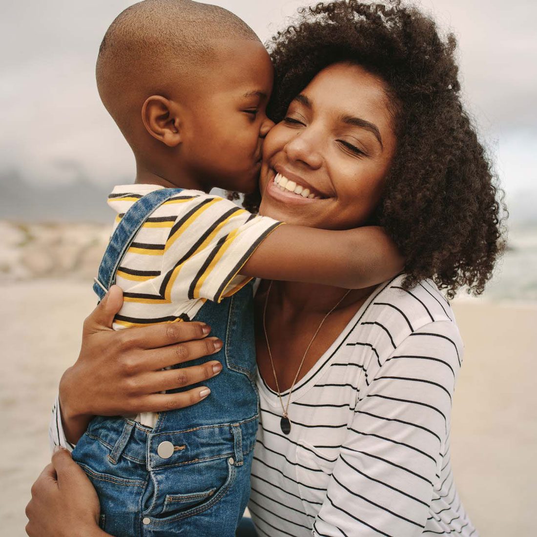 A young child lovingly kisses his adoptive mother on the cheek, a moment of affection in their UK adoption story