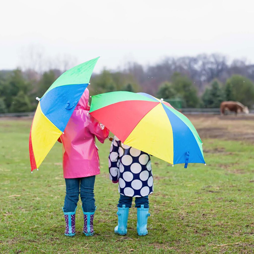 Two children in rain boots holding colourful umbrellas on a rainy day, reflective of the carefree moments in UK child adoption