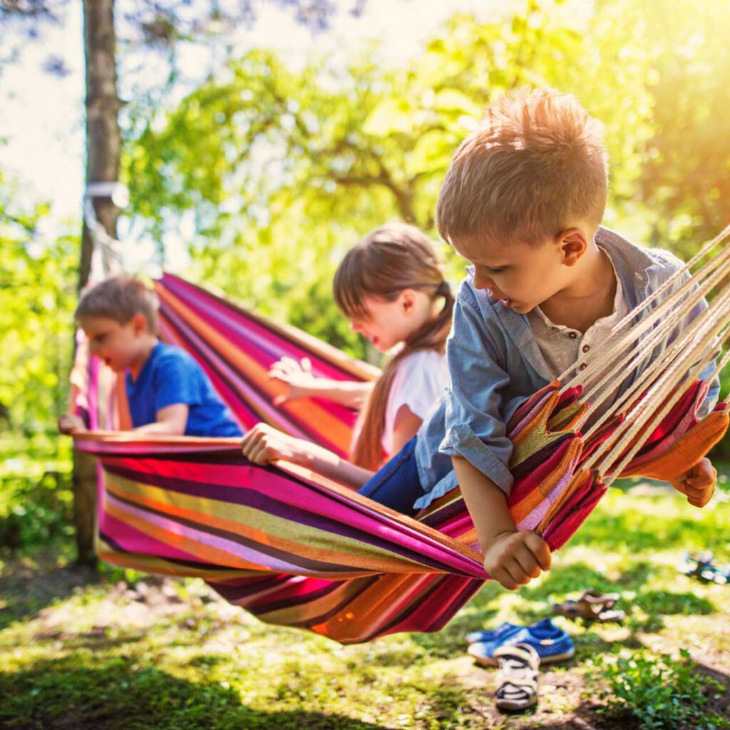 Three children playing together on a colourful hammock in the sunlight, illustrating the joy of siblings in adoption